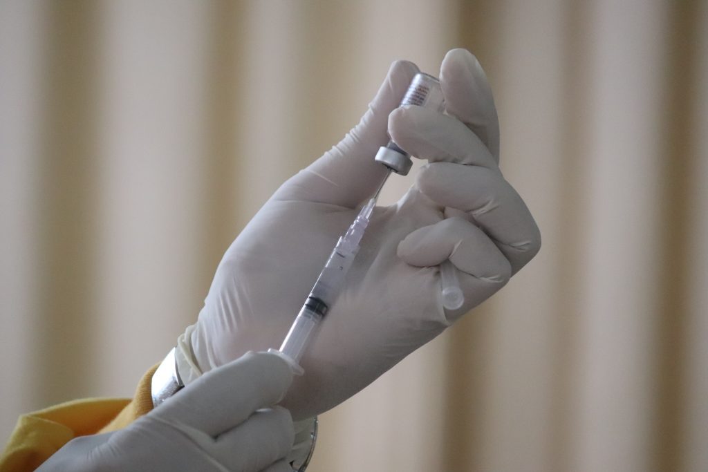 Na imagem podemos ver a mão de um profissional da saúde segurando a seringa de uma vacina da Covid-19